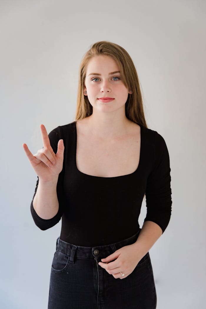 our-story Portrait of a woman in a black blouse using sign language against a white background.