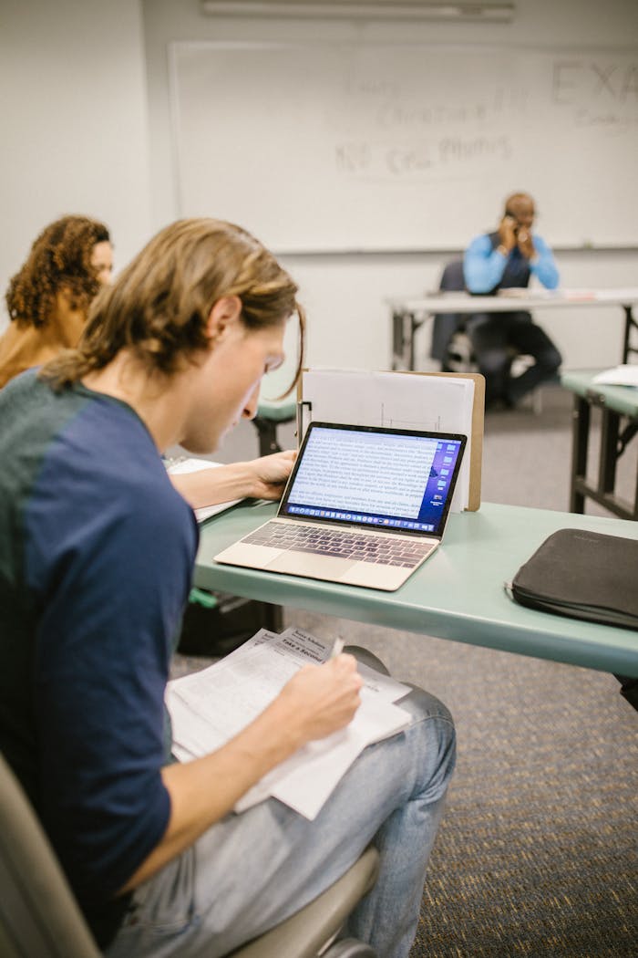 services-03 College student focused on exam preparation in a classroom setting, using a laptop and notes.